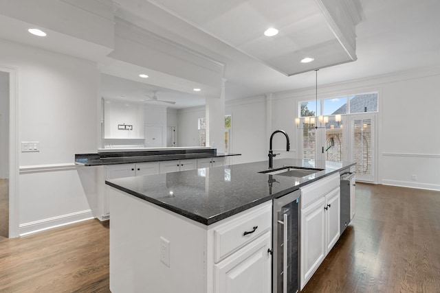 kitchen with a center island with sink, ceiling fan with notable chandelier, sink, wine cooler, and dark stone countertops