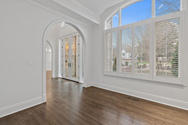 spare room featuring french doors, dark wood-type flooring, crown molding, and a healthy amount of sunlight