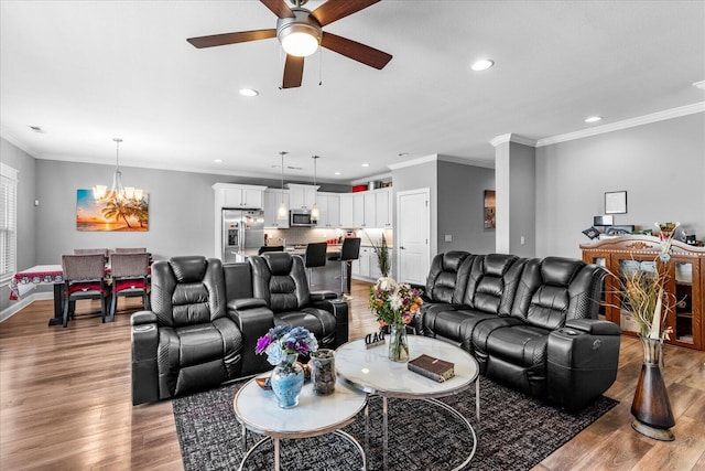 living room with ceiling fan with notable chandelier, light hardwood / wood-style floors, and ornamental molding