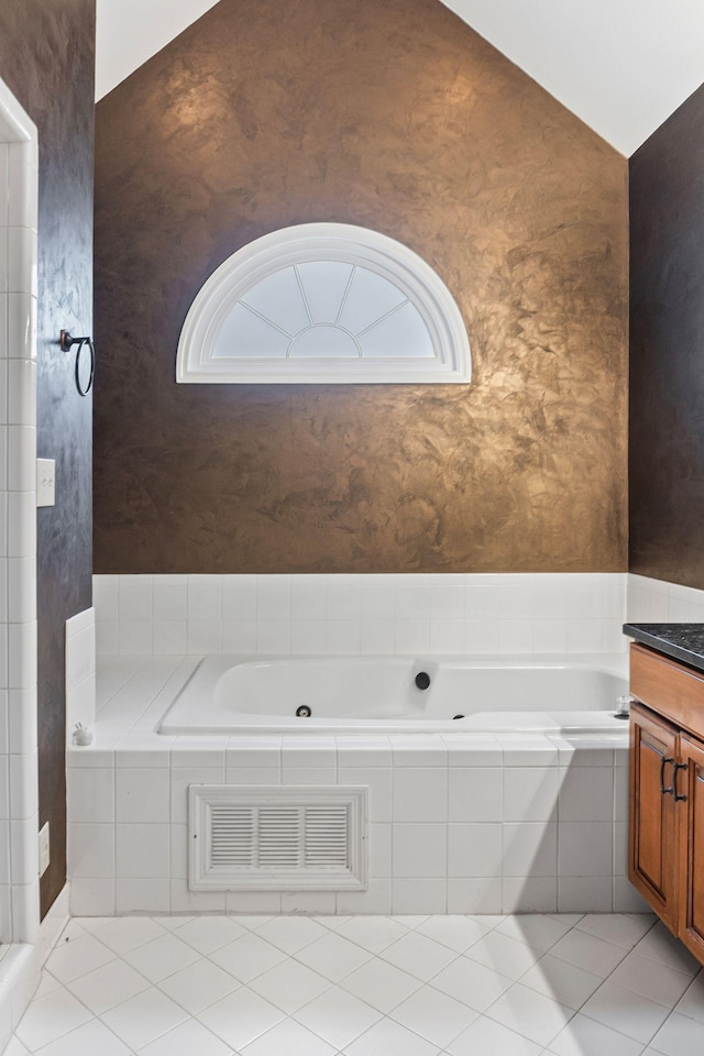 bathroom with tile patterned flooring, vanity, lofted ceiling, and tiled tub