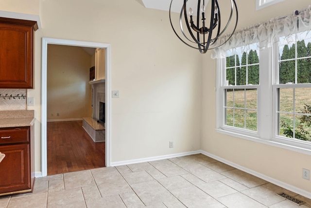 unfurnished dining area with an inviting chandelier, light tile patterned floors, and a fireplace