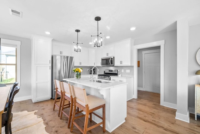 kitchen with white cabinetry, sink, hanging light fixtures, stainless steel appliances, and a center island with sink