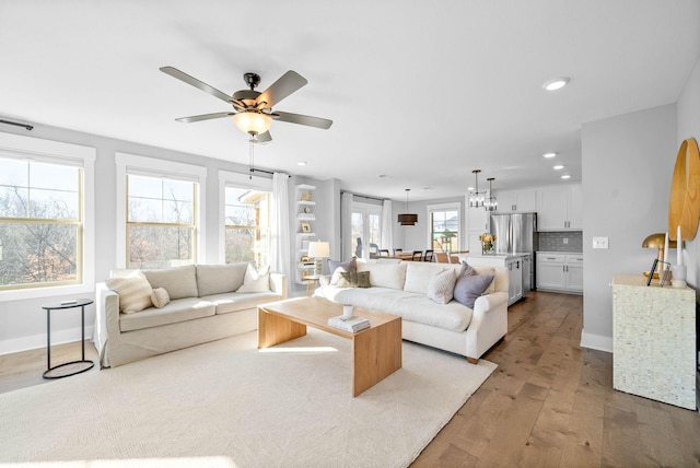 living room featuring ceiling fan with notable chandelier and light hardwood / wood-style floors