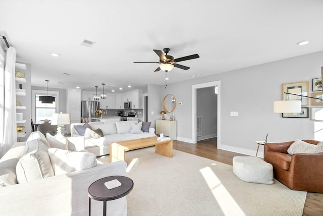 living room with ceiling fan with notable chandelier and light wood-type flooring