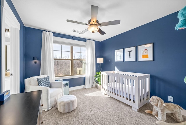 carpeted bedroom with ceiling fan and a nursery area