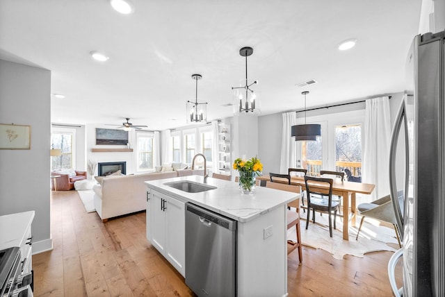 kitchen with sink, stainless steel appliances, an island with sink, pendant lighting, and white cabinets