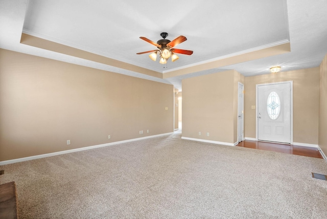 entrance foyer with dark colored carpet, a tray ceiling, ceiling fan, and ornamental molding