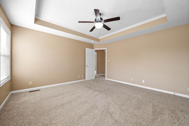 empty room with carpet flooring, ceiling fan, a raised ceiling, and ornamental molding