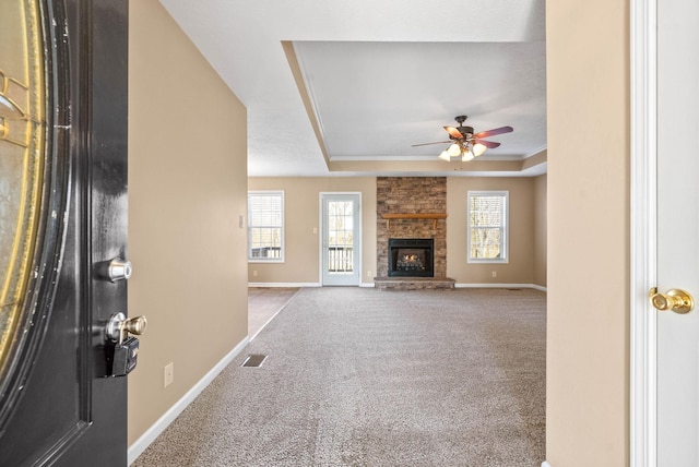 unfurnished living room featuring ceiling fan, a stone fireplace, light colored carpet, and a tray ceiling