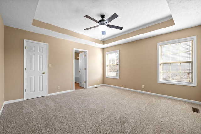 unfurnished bedroom featuring ensuite bath, ceiling fan, and a tray ceiling