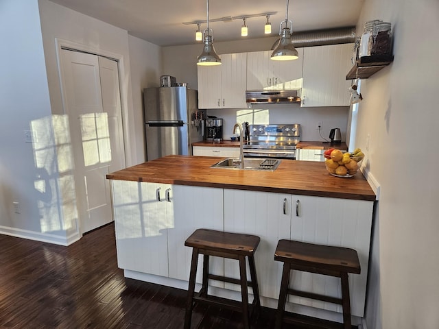 kitchen with appliances with stainless steel finishes, a kitchen breakfast bar, sink, butcher block countertops, and hanging light fixtures