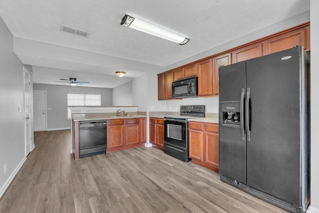 kitchen with kitchen peninsula, light wood-type flooring, ceiling fan, sink, and black appliances