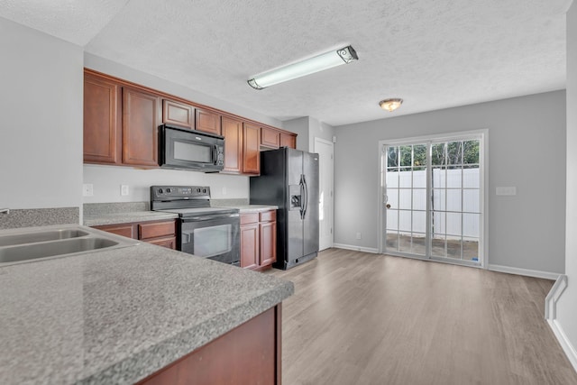 kitchen featuring a textured ceiling, sink, light hardwood / wood-style floors, and black appliances