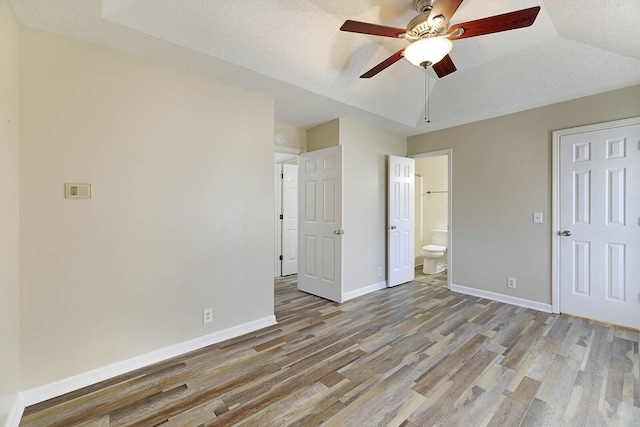 unfurnished bedroom featuring ensuite bathroom, wood-type flooring, lofted ceiling, ceiling fan, and a textured ceiling