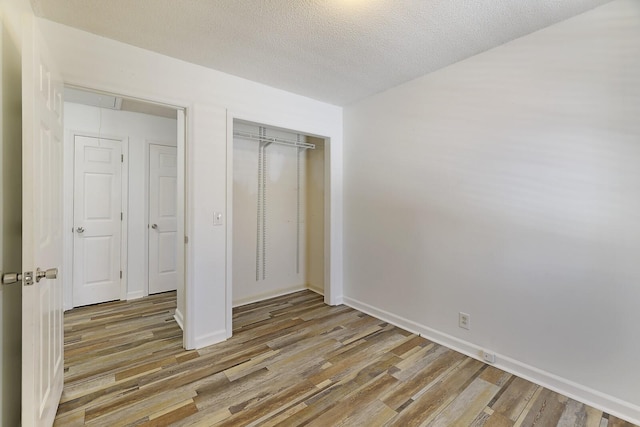 unfurnished bedroom with light wood-type flooring, a textured ceiling, and a closet