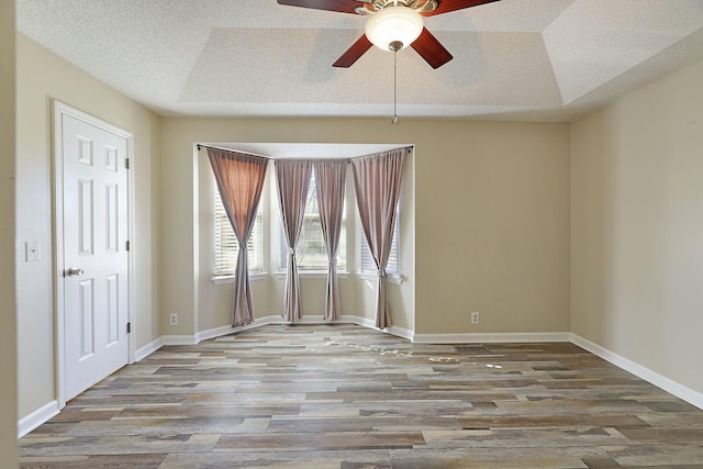 empty room featuring a tray ceiling, wood-type flooring, and ceiling fan