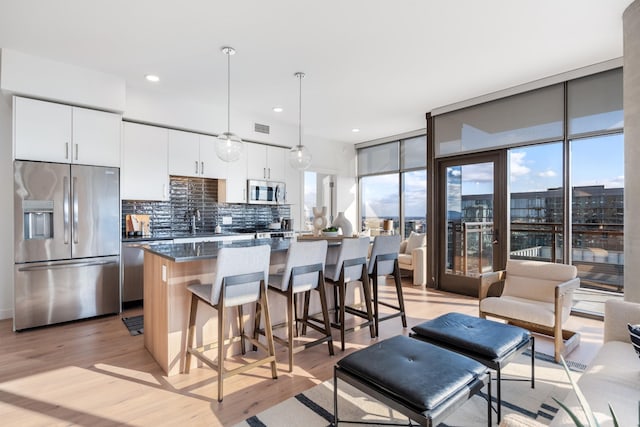 kitchen with white cabinetry, decorative light fixtures, appliances with stainless steel finishes, a kitchen island, and backsplash