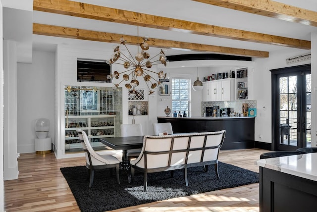 dining space featuring beam ceiling, french doors, a chandelier, and light hardwood / wood-style floors