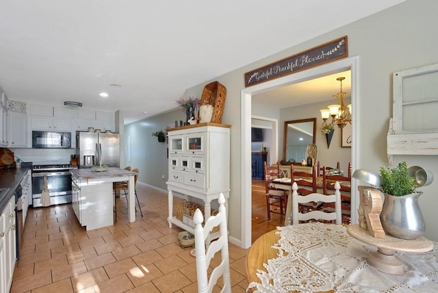 kitchen with a kitchen island, white cabinetry, stainless steel appliances, light tile patterned floors, and a chandelier