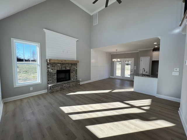 unfurnished living room with dark hardwood / wood-style flooring, ceiling fan with notable chandelier, sink, high vaulted ceiling, and a fireplace