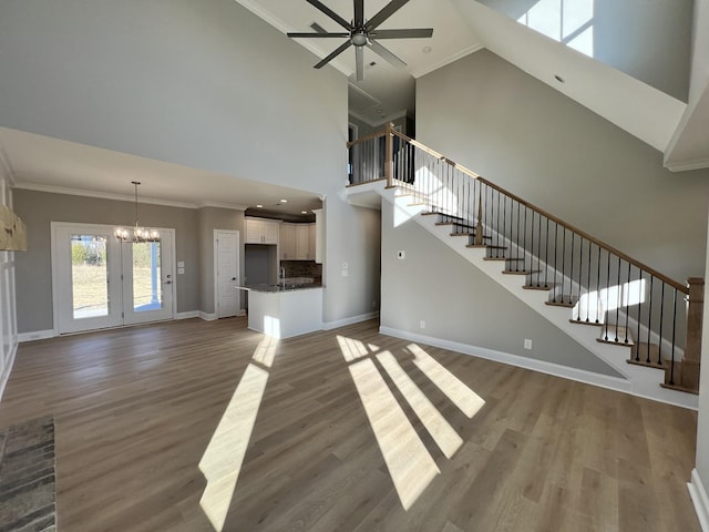 unfurnished living room featuring hardwood / wood-style floors, ceiling fan with notable chandelier, ornamental molding, and a high ceiling