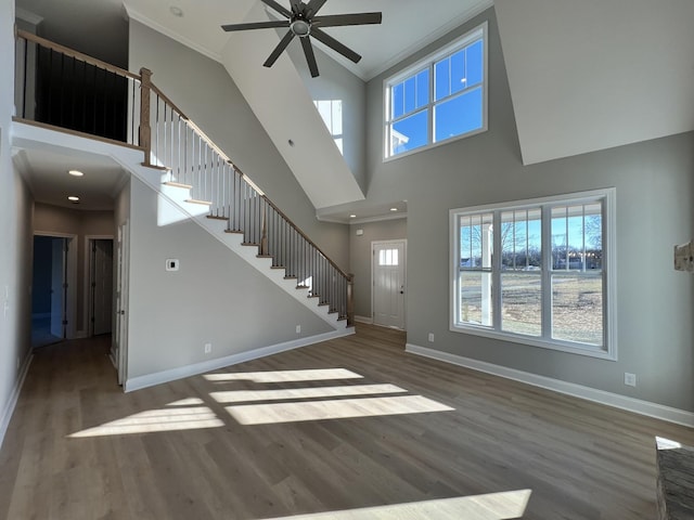 unfurnished living room with ceiling fan, a towering ceiling, wood-type flooring, and ornamental molding