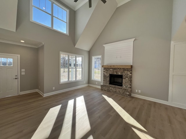 unfurnished living room featuring dark wood-type flooring, ceiling fan, ornamental molding, a fireplace, and a towering ceiling