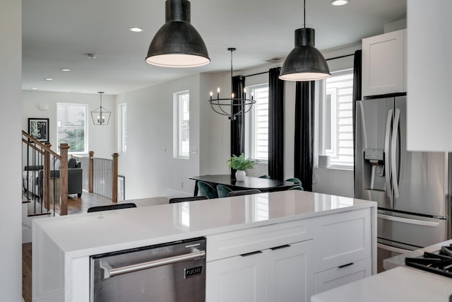 kitchen featuring appliances with stainless steel finishes, a kitchen island, decorative light fixtures, a chandelier, and white cabinetry