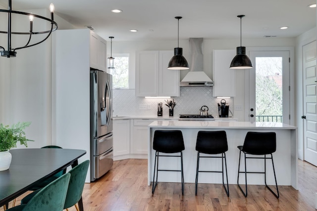 kitchen featuring wall chimney exhaust hood, pendant lighting, stainless steel fridge with ice dispenser, light hardwood / wood-style floors, and white cabinetry