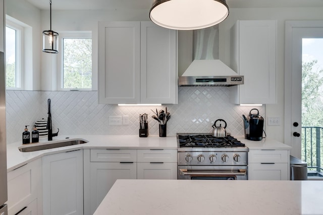 kitchen featuring decorative backsplash, wall chimney exhaust hood, pendant lighting, white cabinets, and stainless steel gas stove