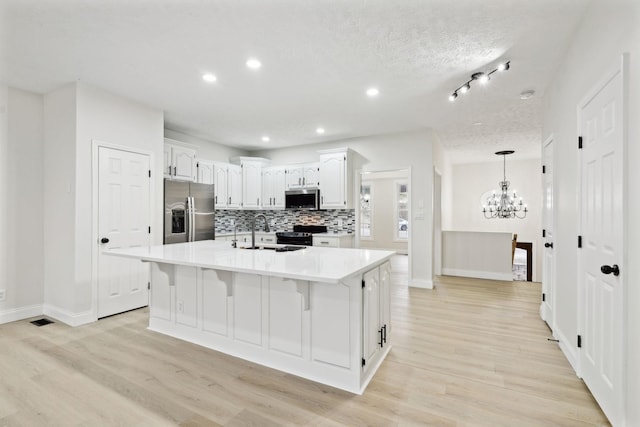 kitchen with a kitchen island with sink, white cabinets, appliances with stainless steel finishes, tasteful backsplash, and a chandelier