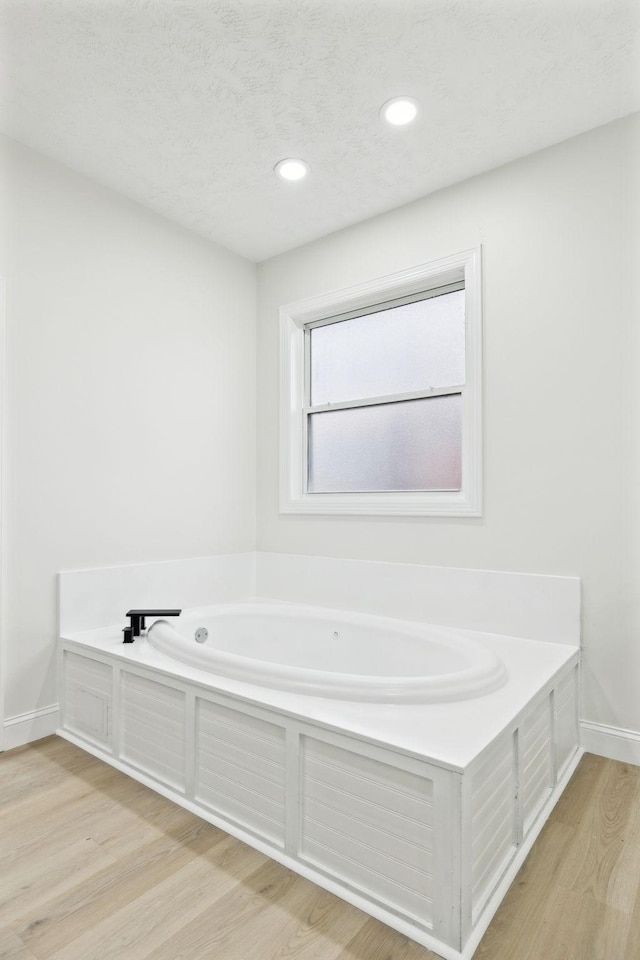 bathroom with wood-type flooring, a textured ceiling, and a tub