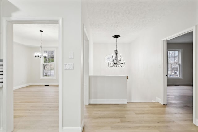 hall with light wood-type flooring, a textured ceiling, and a chandelier