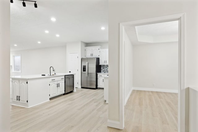 kitchen with tasteful backsplash, white cabinetry, light hardwood / wood-style flooring, and stainless steel appliances