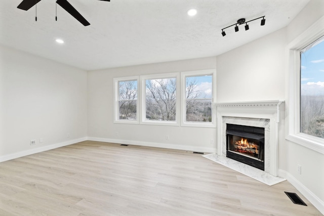 unfurnished living room featuring plenty of natural light, a premium fireplace, light hardwood / wood-style flooring, and track lighting