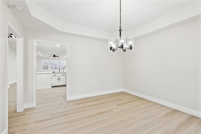 unfurnished dining area with a raised ceiling, light hardwood / wood-style flooring, ceiling fan with notable chandelier, and sink