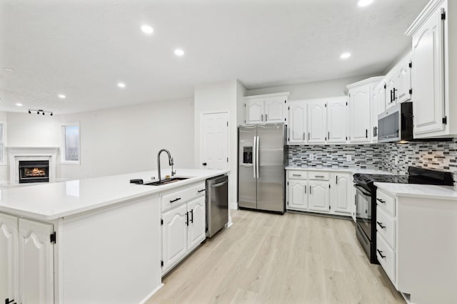 kitchen with appliances with stainless steel finishes, light wood-type flooring, sink, a center island with sink, and white cabinetry