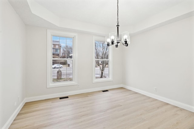 unfurnished dining area with a tray ceiling, a chandelier, and light hardwood / wood-style floors