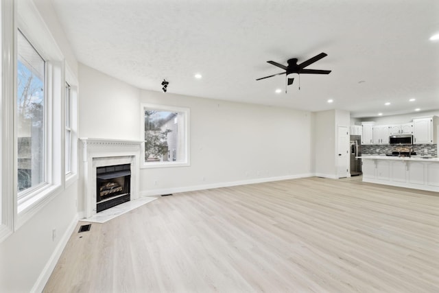 unfurnished living room featuring ceiling fan, a high end fireplace, and light hardwood / wood-style flooring