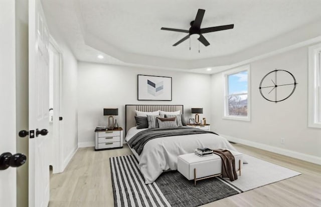 bedroom with a tray ceiling, ceiling fan, and light hardwood / wood-style flooring