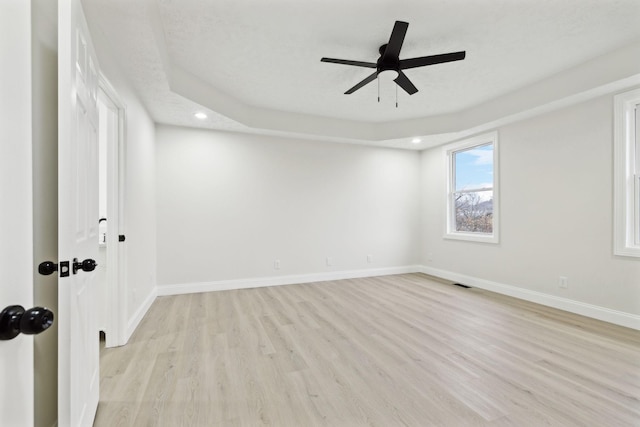 empty room featuring light wood-type flooring, a tray ceiling, and ceiling fan