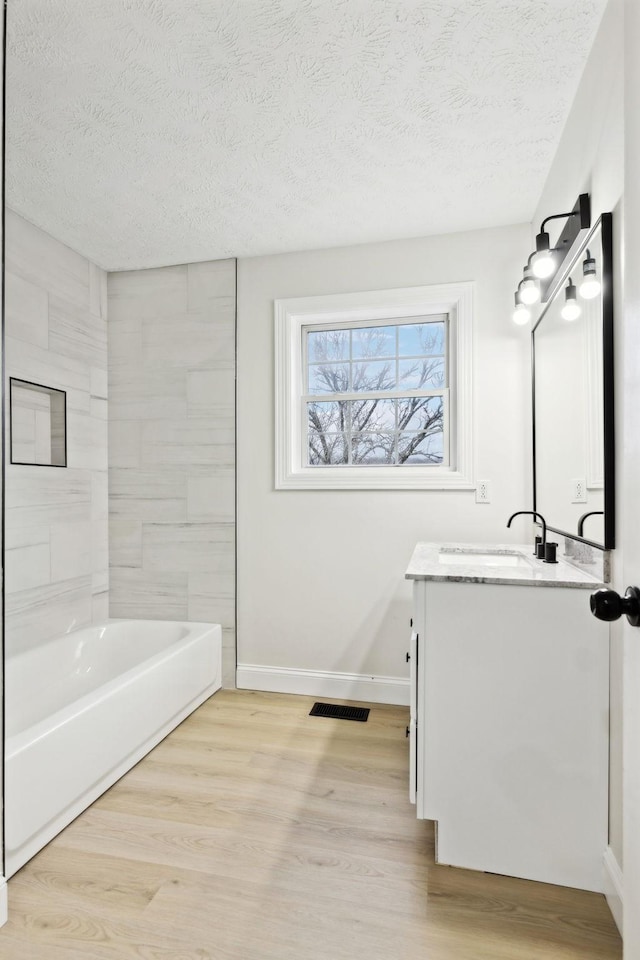 bathroom featuring hardwood / wood-style flooring, vanity, a textured ceiling, and tiled shower / bath