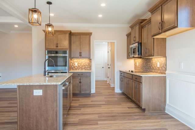 kitchen with stainless steel appliances, tasteful backsplash, an island with sink, pendant lighting, and light wood-type flooring