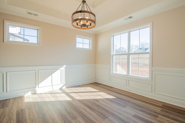 empty room featuring a notable chandelier, a raised ceiling, light wood-type flooring, and crown molding