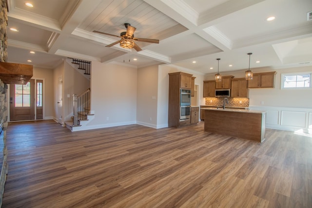 kitchen with appliances with stainless steel finishes, dark hardwood / wood-style flooring, light stone counters, hanging light fixtures, and an island with sink