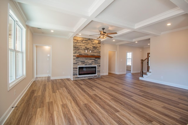 unfurnished living room featuring ceiling fan, coffered ceiling, a stone fireplace, beamed ceiling, and hardwood / wood-style flooring