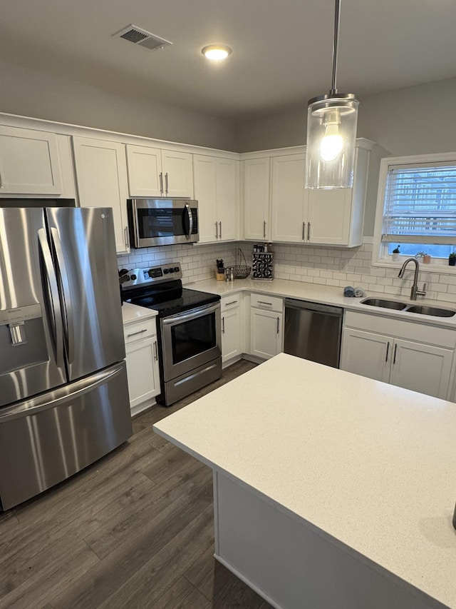 kitchen featuring dark wood-type flooring, sink, white cabinetry, decorative light fixtures, and appliances with stainless steel finishes