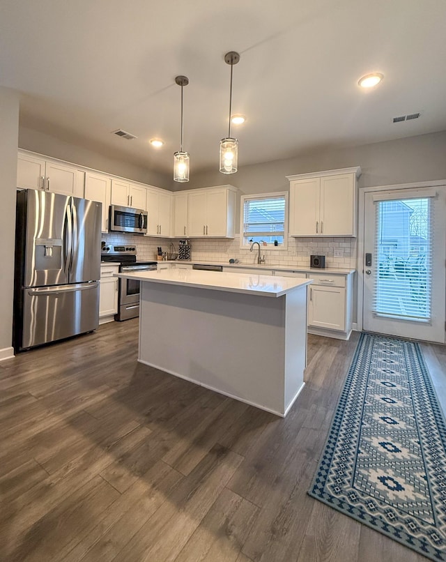 kitchen with pendant lighting, white cabinetry, dark hardwood / wood-style flooring, a center island, and stainless steel appliances