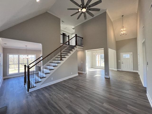 unfurnished living room with dark hardwood / wood-style flooring, ceiling fan with notable chandelier, a wealth of natural light, and ornamental molding