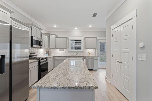 kitchen featuring gray cabinetry, a kitchen island, light stone counters, and appliances with stainless steel finishes